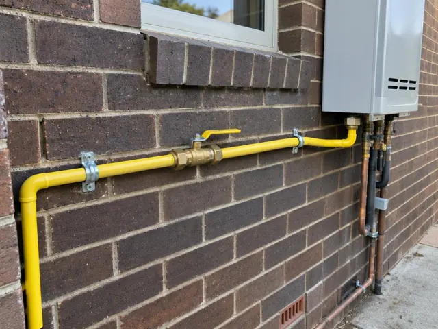 Yellow gas pipe with valve on a brick exterior wall beside a window in Homebush