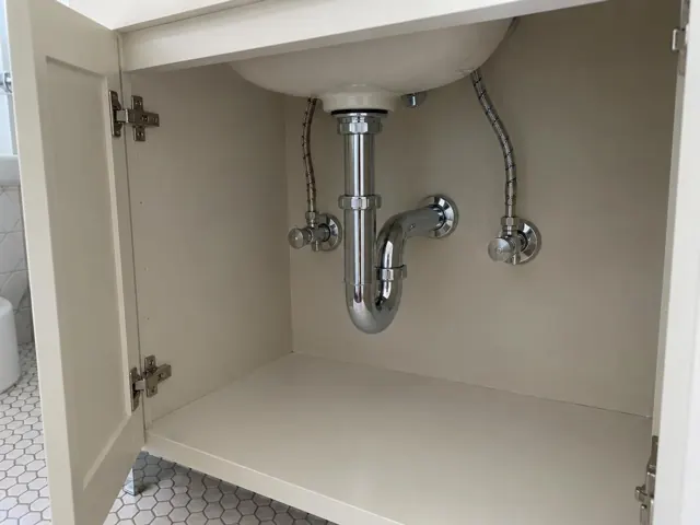Open under-sink cabinet with neat access panel and chrome drain plumbing on a dry wall in Strathfield