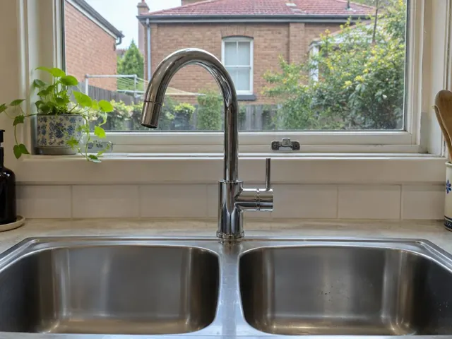 Chrome kitchen mixer tap over a double stainless sink beneath a window in a tiled home kitchen in Ashfield